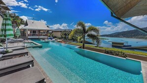 A resort pool area with lounge chairs, a water slide, and a view of the surrounding landscape. - Paradise Palms (Airlie Beach)