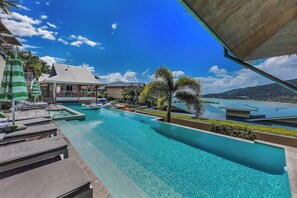 A resort pool area with lounge chairs, a water slide, and a view of the surrounding landscape. - Paradise Palms (Airlie Beach)