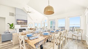 A spacious dining area with a long wooden table set for a meal, surrounded by wooden chairs. - Oceanfront Luxury Panoramic 6BR, Pool, Hot Tub, Game Room, Surf House OBX (Salvo)