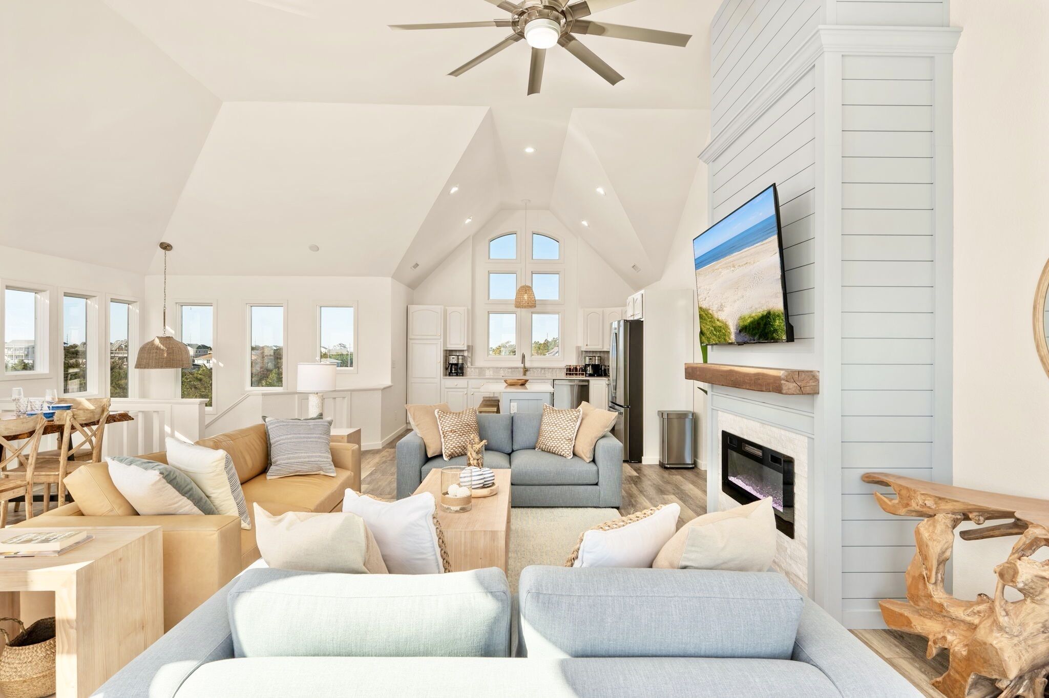 A spacious living room with a high ceiling, a fireplace, and a television mounted on the wall.
