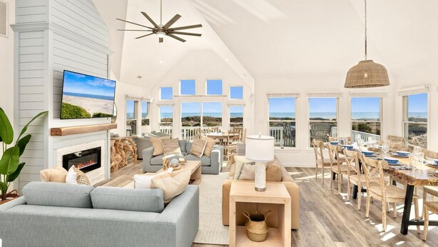 A spacious living room with a fireplace, a television, and a dining area with a view of the ocean. - Oceanfront Luxury Panoramic 6BR, Pool, Hot Tub, Game Room, Surf House OBX (Salvo)