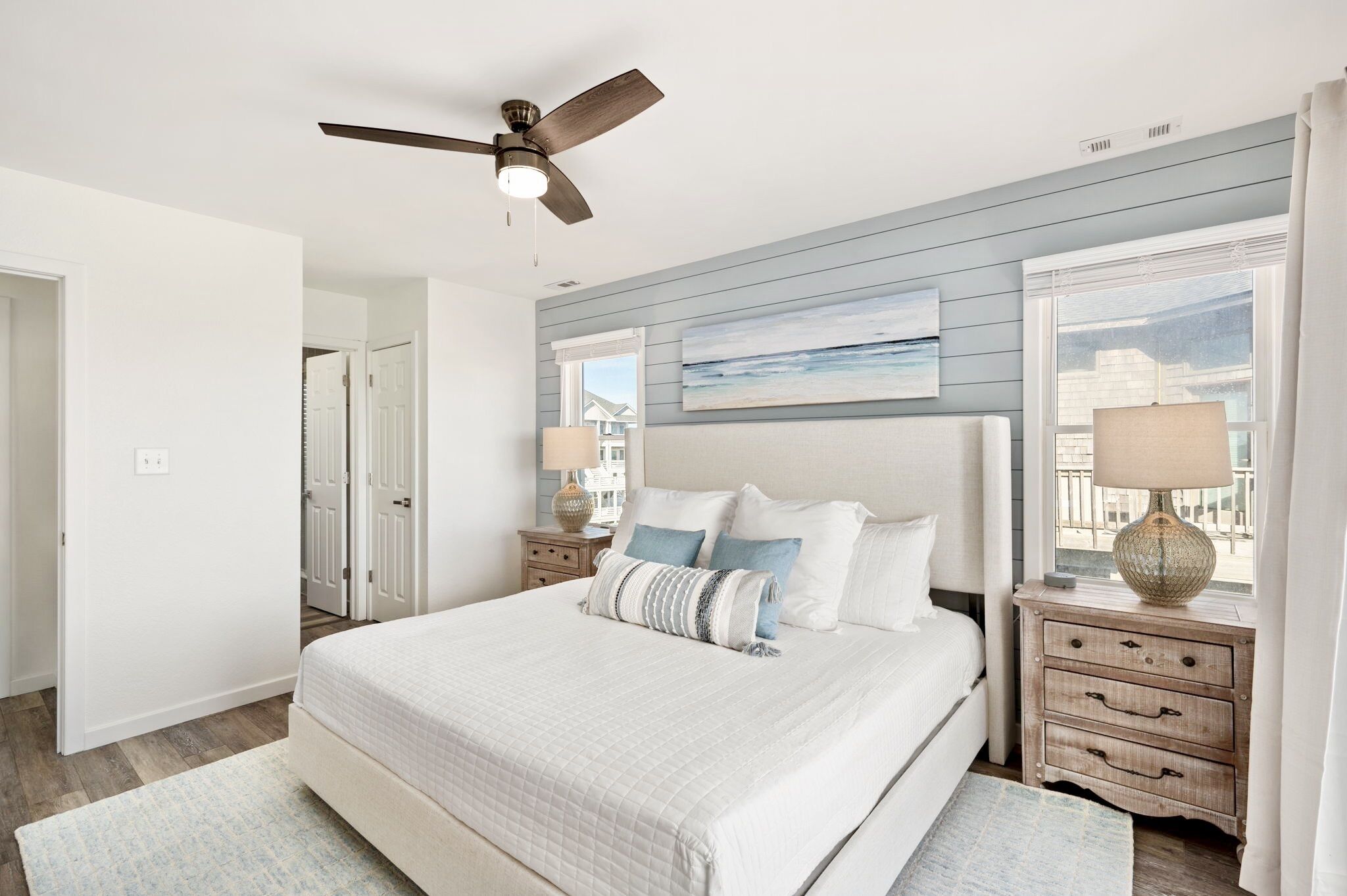 A bedroom with a large bed, a ceiling fan, a nightstand with a lamp, and a window with a view of buildings.