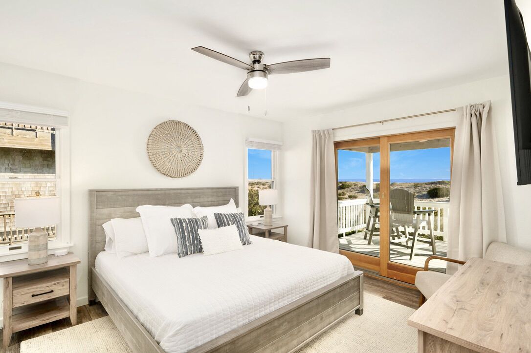 Une chambre avec un lit, un ventilateur de plafond, une vue sur l’extérieur et un balcon équipé d’une table et de chaises.