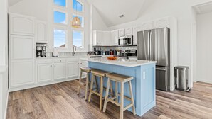 A spacious kitchen with white cabinets, a blue island, stainless steel appliances, and wooden stools. - Oceanfront Luxury Panoramic 6BR, Pool, Hot Tub, Game Room, Surf House OBX (Salvo)