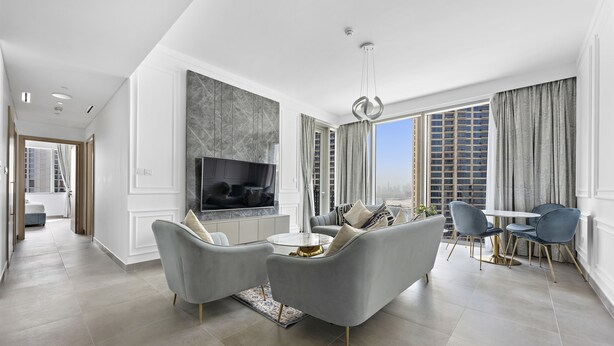 A modern living room with a grey sofa set, a TV, and a dining area with a table and chairs.