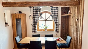 Un comedor con mesa de madera y cuatro sillas, una ventana con cortinas a cuadros y una pared de madera rústica.