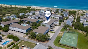 Vue aérienne d’un quartier résidentiel avec des maisons, un court de tennis et une plage en arrière-plan.