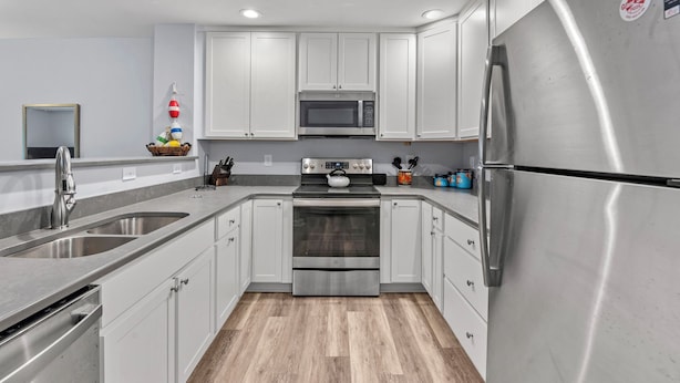 Une cuisine moderne dotée d’appareils électroménagers en acier inoxydable, de meubles blancs et d’un plancher en bois.