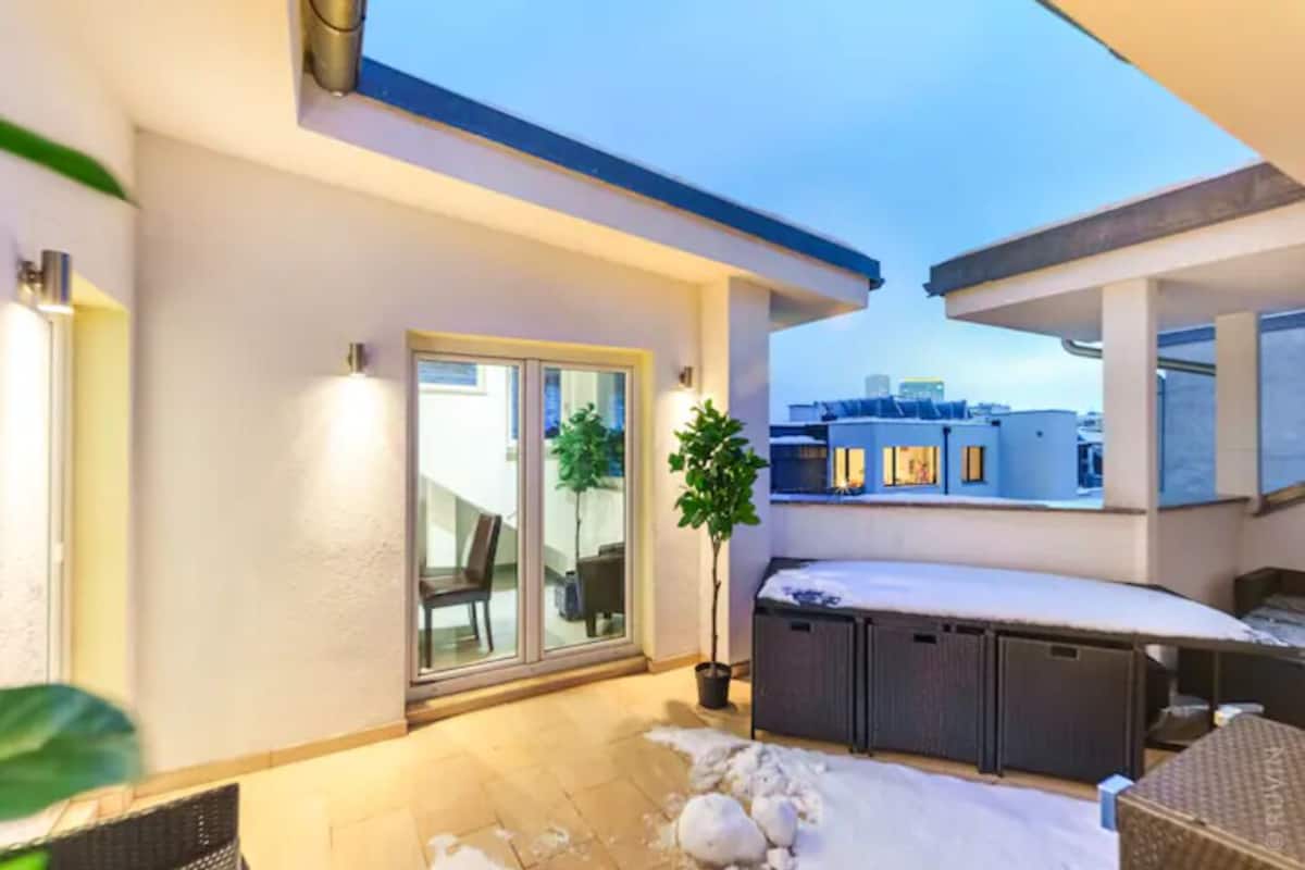 A rooftop terrace with a glass door leading to a balcony, a potted plant, and a snow-covered floor.