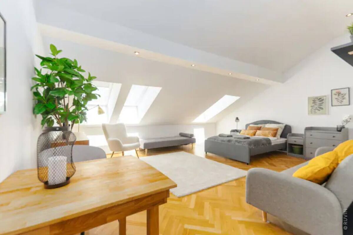 A modern loft apartment with a dining area, a gray sofa, a gray armchair, and a small table with a plant.