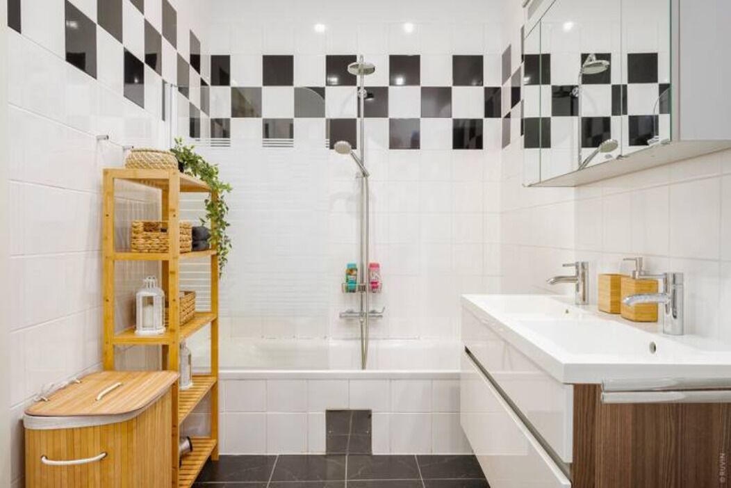 A modern bathroom with a checkered tile backsplash, a freestanding shower, a wooden vanity with a sink, and a shelf with toiletries.