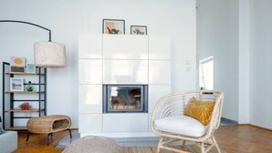 A modern living room with a white fireplace, wicker furniture, and a large window. - Designer Apartments - Near Reumannplatz (Vienna)