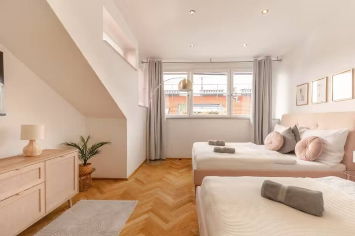 A bedroom with two beds, a wooden dresser, a plant, and a view of the outside.