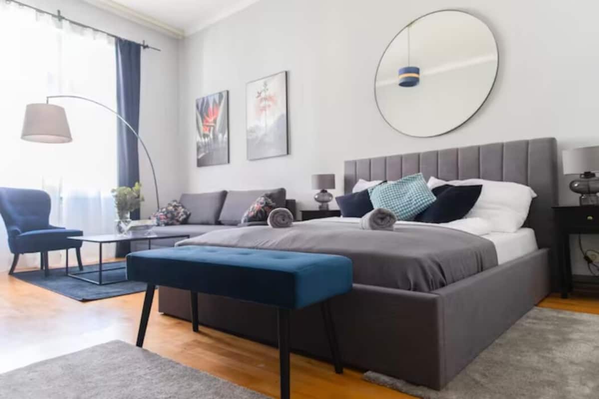 A modern bedroom with a large bed, a round mirror, and a blue bench.