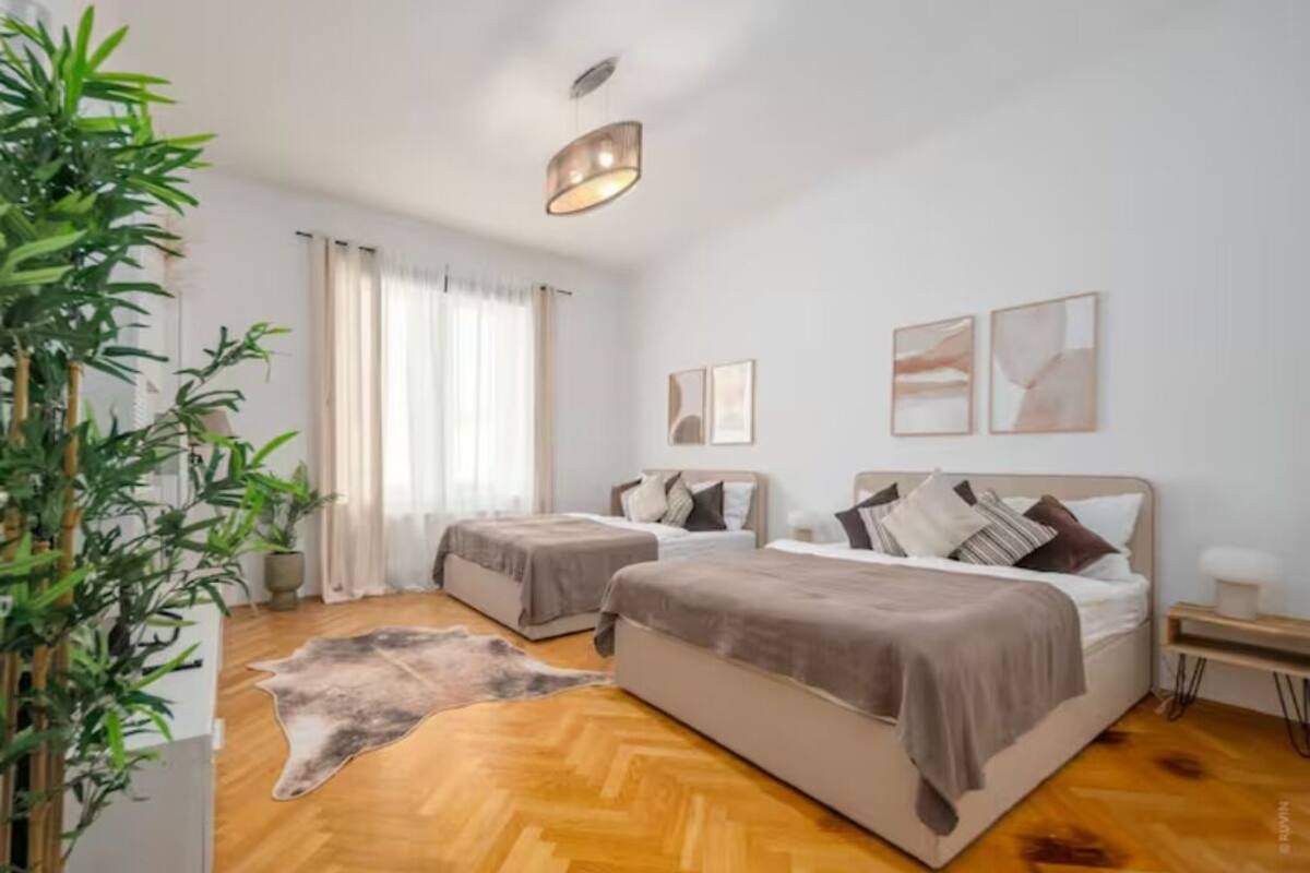 A hotel room with two beds, a wooden floor, a large plant, and artwork on the wall.
