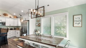 A modern kitchen with white cabinets, a wooden dining table, and a chandelier. - Irie: New Build | Private Pool | Hot Tub (Corolla)