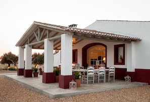 A covered outdoor seating area with tables and chairs, a white building with red accents, and potted plants. - Herdade Quinta da Chamine (Ferreira do Alentejo)