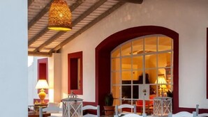 A cozy outdoor seating area with a table and chairs, a hanging light fixture, and a large window with red trim.