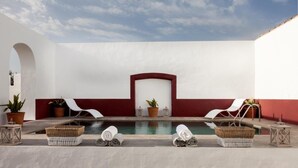 A pool area with two lounge chairs, a small pool, and potted plants.