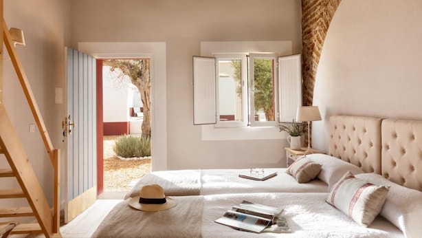 A bedroom with a bed, a nightstand, a lamp, and a window with a view of the outside.