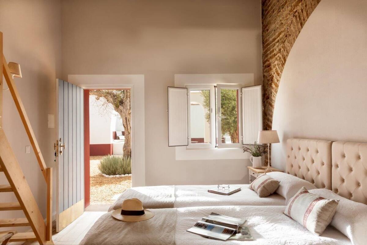 Un dormitorio con una cama, una mesita de noche, una lámpara y una ventana que ofrece vistas al exterior.