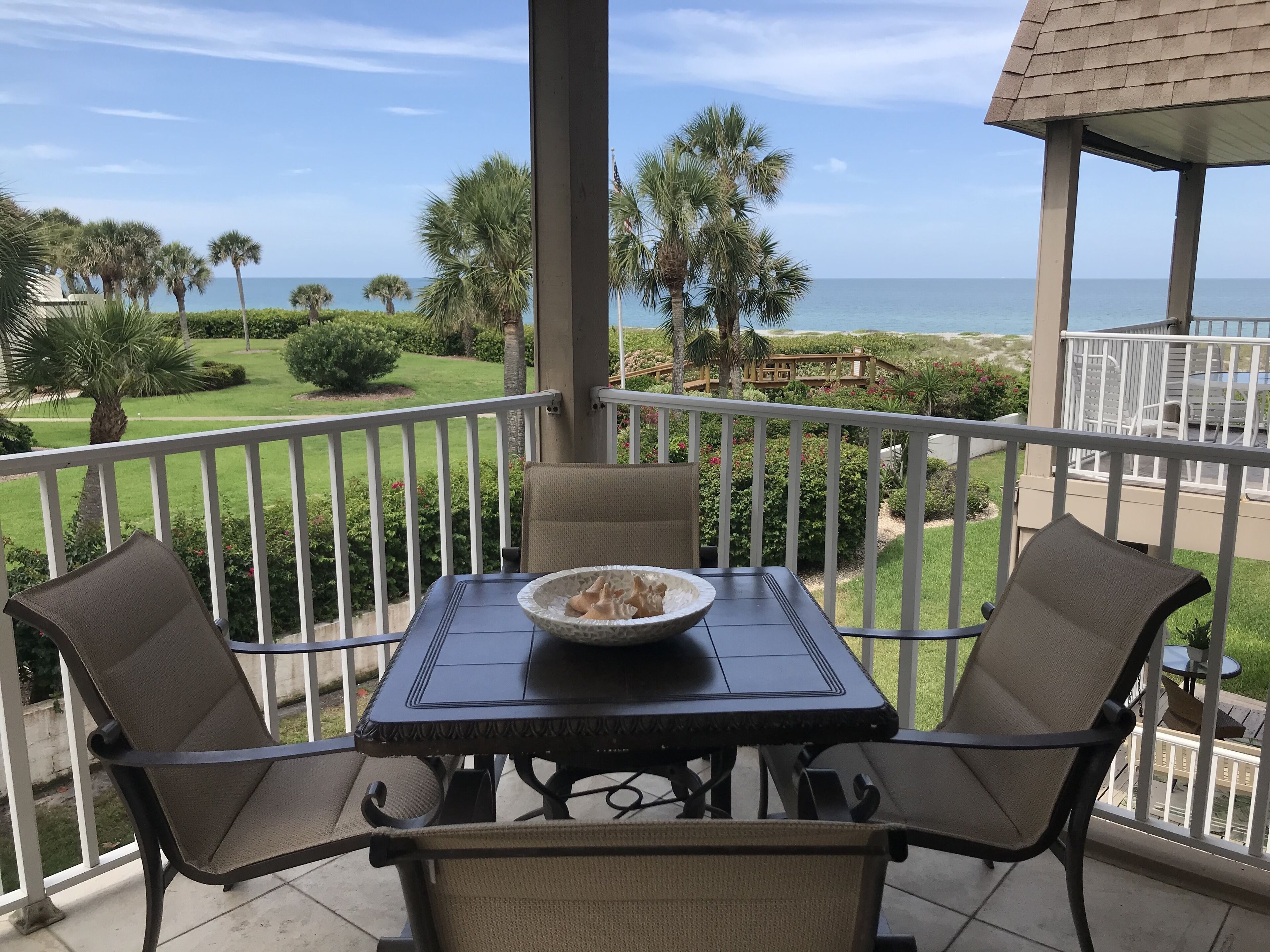 A balcony with a table and chairs, overlooking a beach and a golf course.