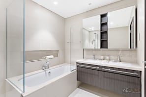 A modern bathroom with a glass shower enclosure, a freestanding bathtub, and a vanity with a large mirror. - WelHome - Cozy 3BR With Maids Room & Access to Dubai Mall  (Dubai)
