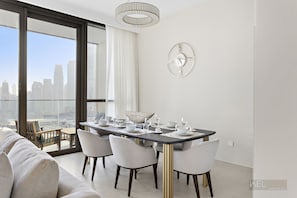 A modern dining area with a large table set for six, a city view through floor-to-ceiling windows, and a minimalist decor. - WelHome - Cozy 3BR With Maids Room & Access to Dubai Mall  (Dubai)