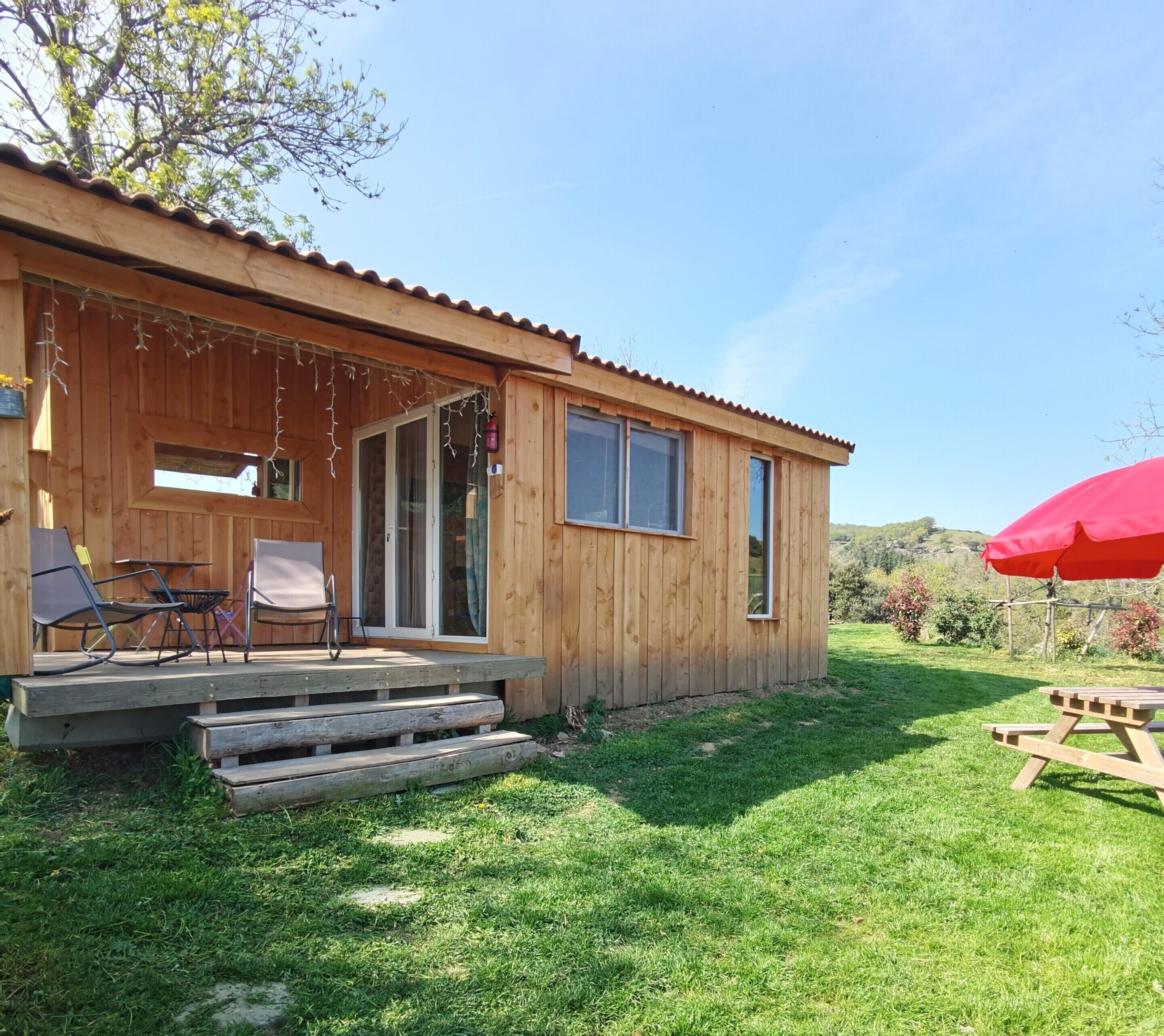 A wooden cabin with a porch, a table, and chairs.
