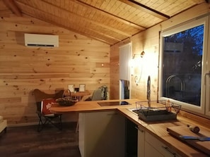 A cozy cabin interior with a wooden interior, a dining area, a kitchen with a sink, and a window with a view of the outdoors.