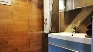 A bathroom with a wooden wall, a white bathtub, a blue vanity with a mirror, and a shower with a handheld showerhead. - Farm cottage with view of the Vercors 4 pers (Saint-Péray)