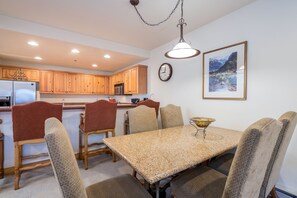 A dining area with a granite table and wooden chairs, a kitchen with wooden cabinets, and a framed landscape painting on the wall. - Bear Creek Lodge 109a 1 Bedroom Condo by Alpine Lodging Telluride (Telluride)