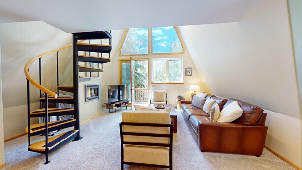 Un loft spacieux doté d’un escalier en colimaçon, d’un salon confortable avec un canapé et une télévision, et de grandes fenêtres offrant une vue sur l’extérieur.