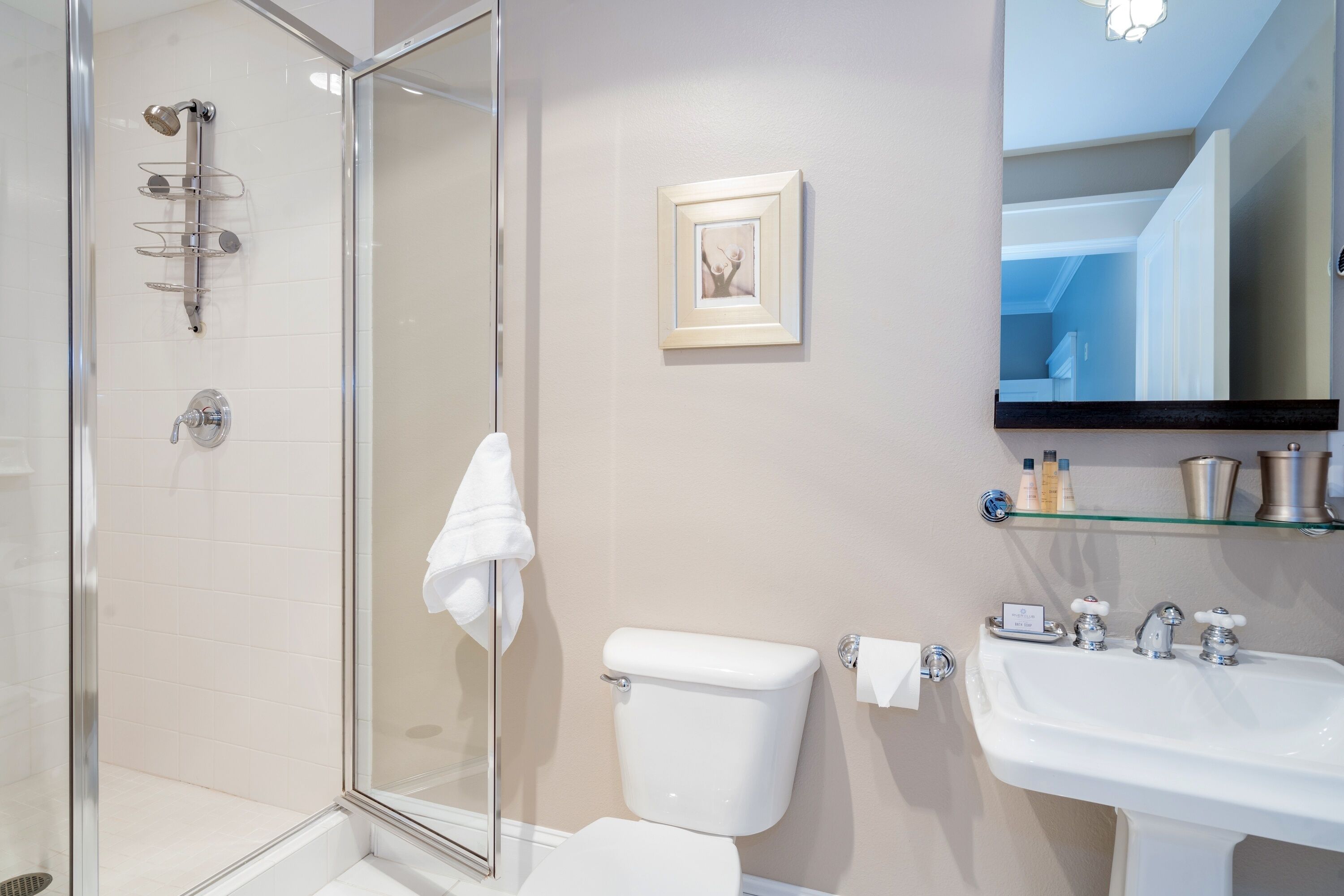A bathroom with a glass shower enclosure, a toilet, a sink, and a framed picture on the wall.