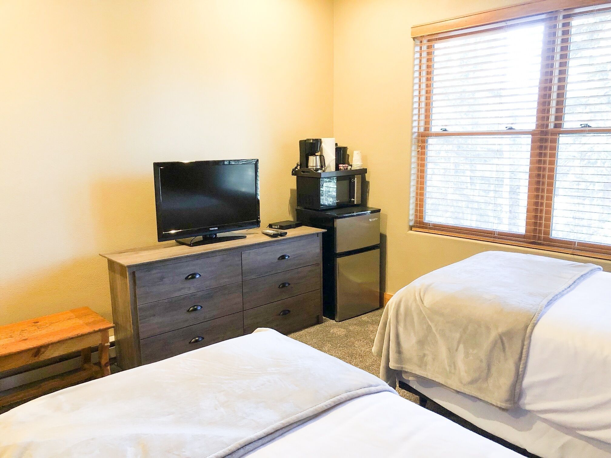 A hotel room with a bed, a TV on a dresser, a microwave, and a window with blinds.