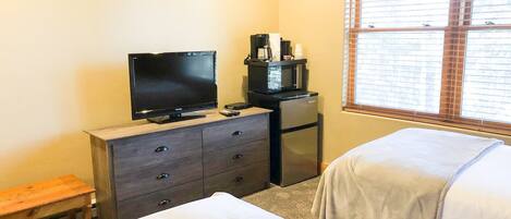 A hotel room with a bed, a TV on a dresser, a microwave, and a window with blinds.