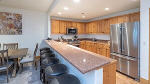 A modern kitchen with wooden cabinets, stainless steel appliances, a granite countertop, and a dining area with a wooden table and bar stools.