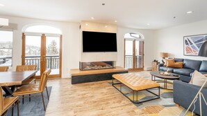A spacious living room with a fireplace, a large TV, a sofa, and a dining area with chairs.