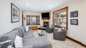 Ein modernes Wohnzimmer mit einem grauen Ecksofa, einem grauen Sessel, einem Couchtisch und einem Kamin.