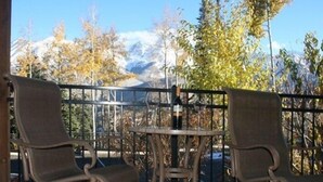 Ein Balkon mit zwei Stühlen und einem Tisch, mit Blick auf ein Bergmassiv im Herbstlaub.