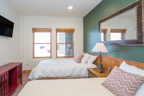 Une chambre avec deux lits, une télévision, un miroir et une fenêtre donnant sur un immeuble.