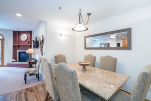 Un coin repas comprenant une table en granit, quatre chaises rembourrées, un buffet en bois, un téléviseur et une cheminée.