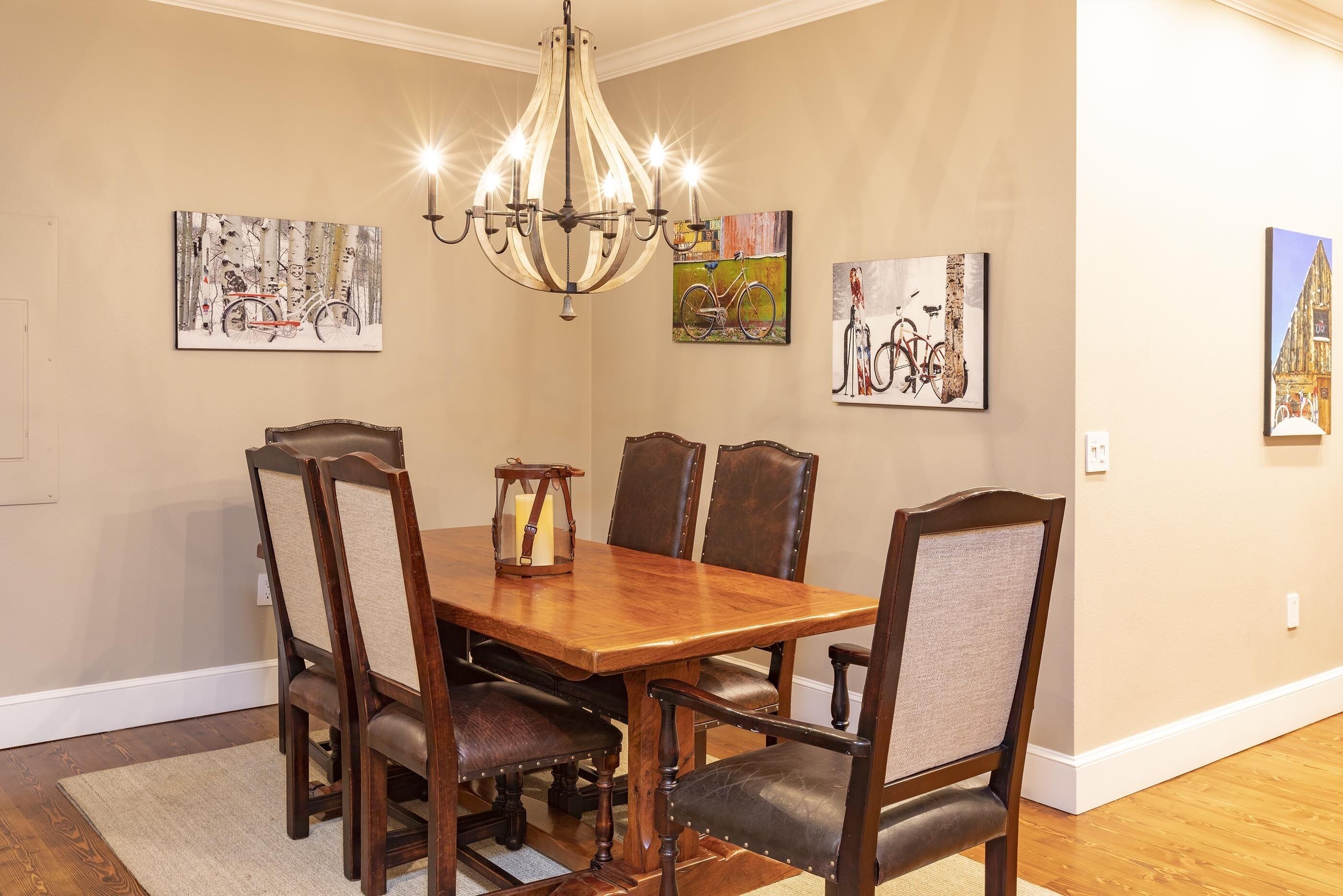Comedor con mesa y sillas de madera, una lámpara de araña y decoración en las paredes.
