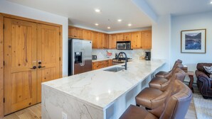 A modern kitchen with wooden cabinets, a marble island, and a seating area with leather chairs. - Bear Creek Lodge 211 1 Bedroom Condo by Alpine Lodging Telluride (Telluride)