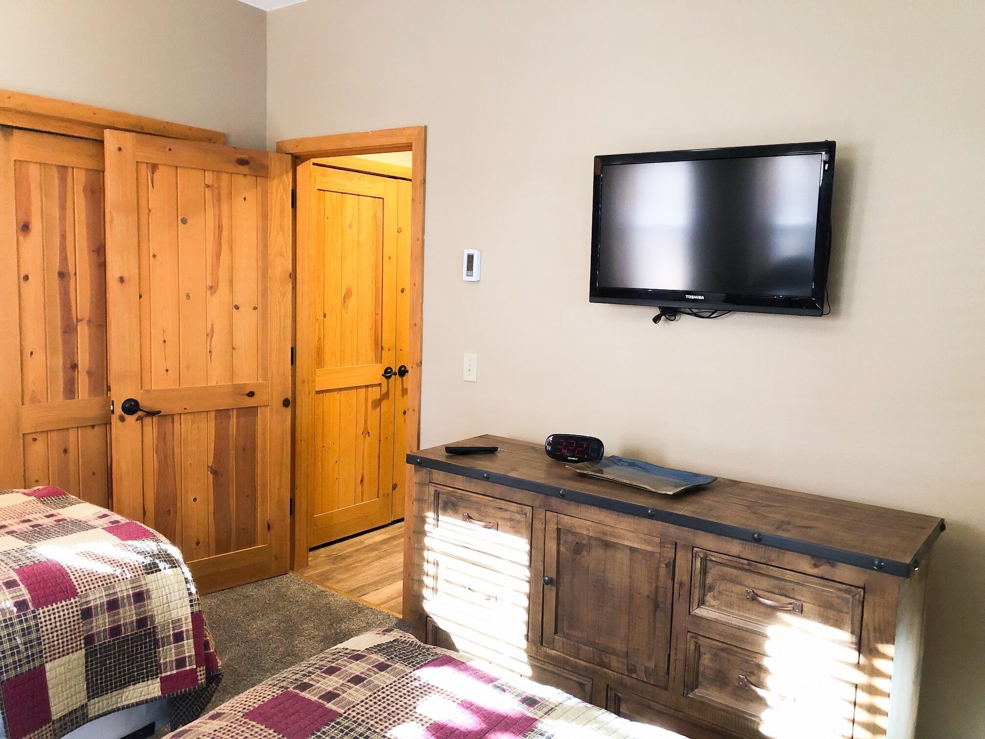 A bedroom with wooden doors, a TV, a dresser, and a bed with a checkered blanket.