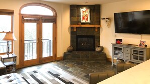 A living room with a fireplace, a television, and a stone floor.