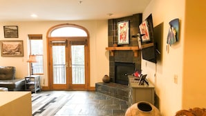 A living room with a fireplace, a large window, and a stone floor.