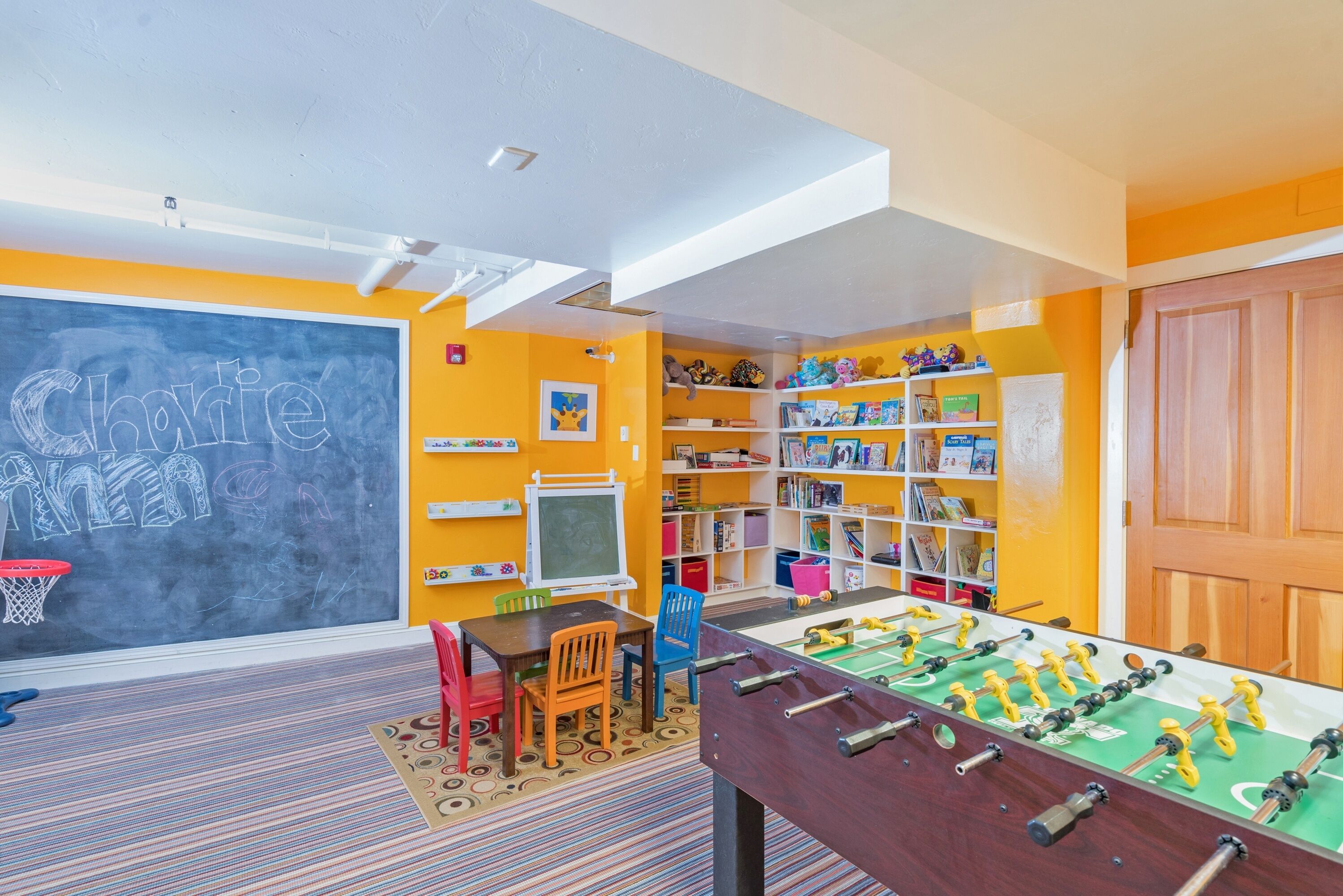 Une salle de jeux pour enfants avec un baby-foot, un tableau noir orné de dessins et des étagères remplies de jouets et de livres.