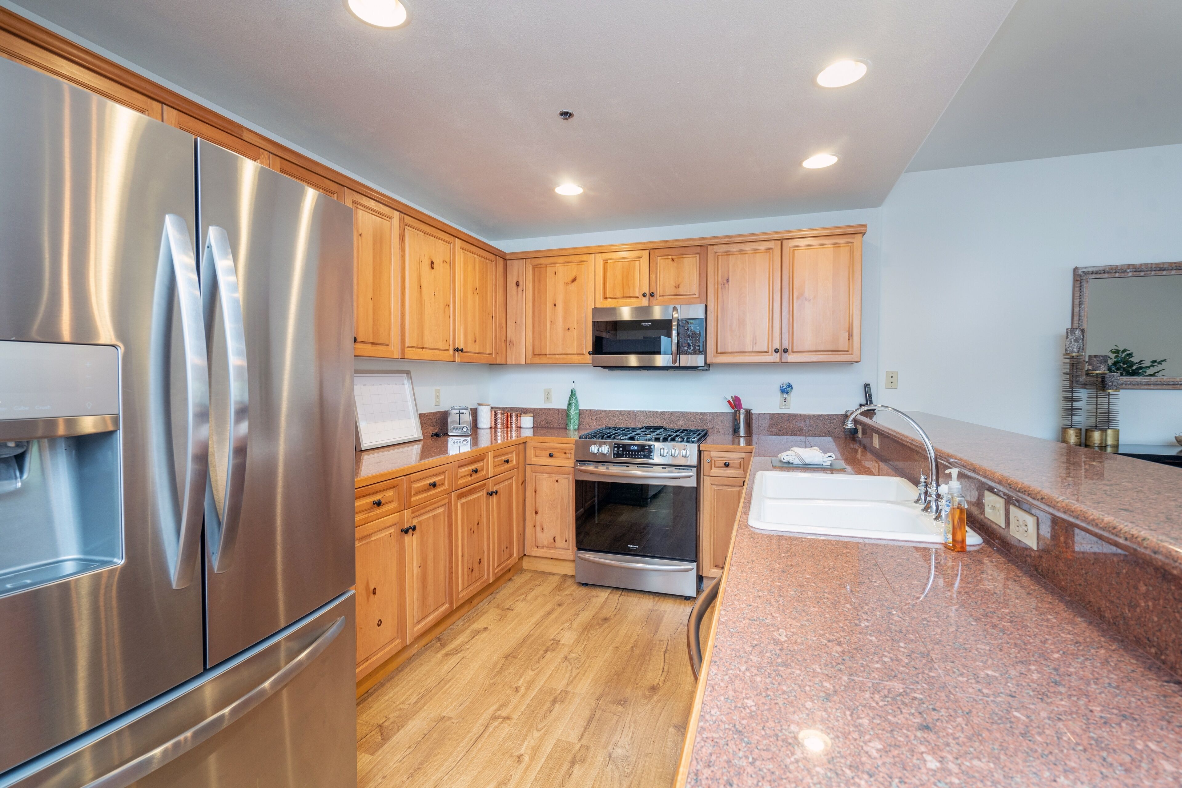 A modern kitchen with stainless steel appliances, wooden cabinets, granite countertops, and a built-in oven.