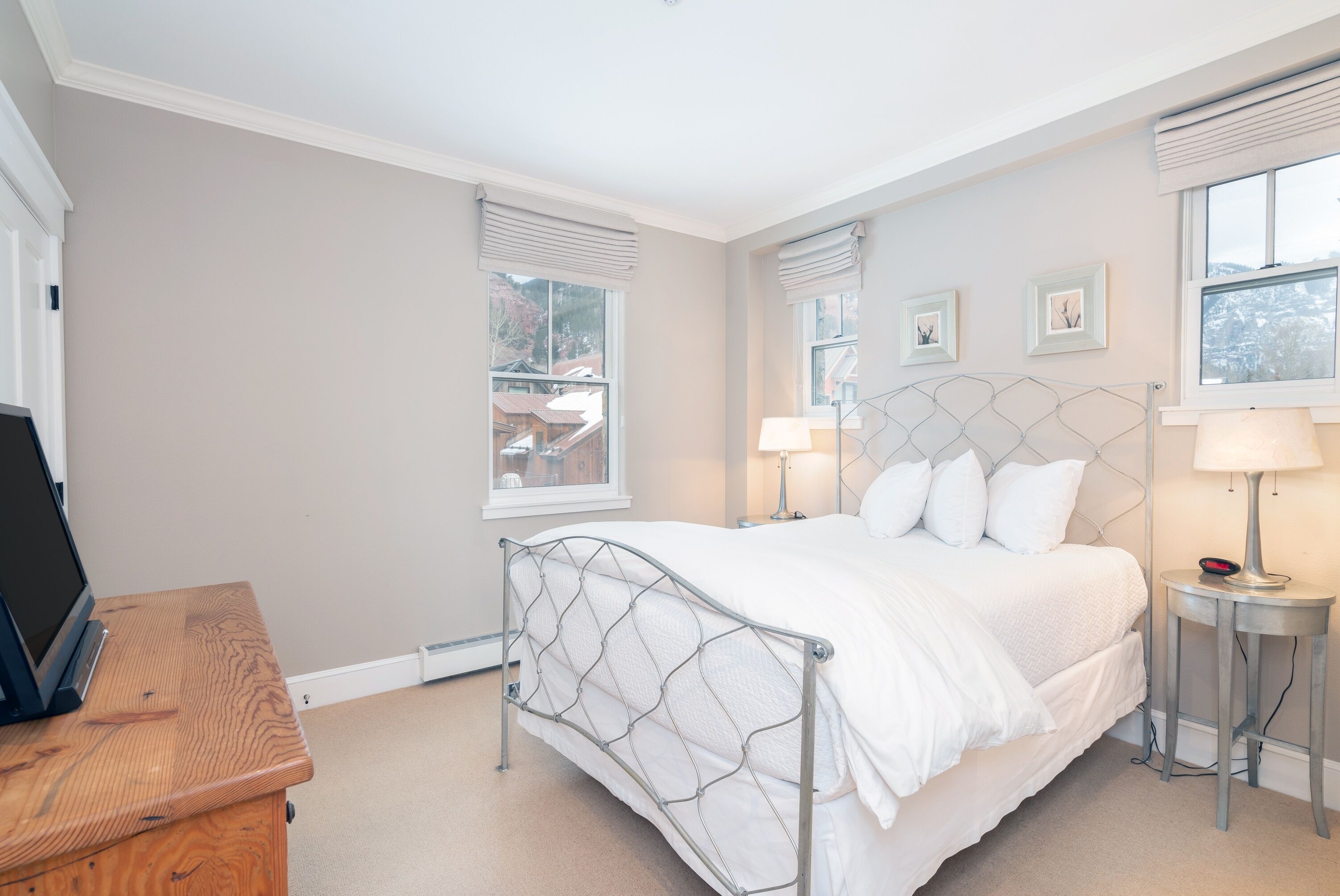 A bedroom with a bed, bedside lamps, a desk, and a window with blinds.